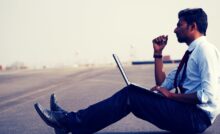 Indian man in white shirt and black trousers and tie sitting on the street with laptop